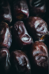 A vertical, extreme close-up shot of several dark, textured dates on a rich, dark background in India, showcasing their natural detail.