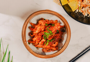 Overhead shot of a wooden bowl filled with spicy, saucy chicken, garnished with green onions.