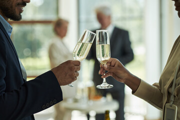 Caucasian middle aged man and Black woman clinking champagne glasses during social gathering, two senior adults conversing in background, celebrating special occasion indoors