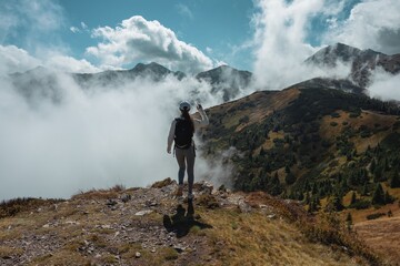 Kobieta stojąca na szczycie góry i podziwiająca panoramę gór i chmur, wędrówka wśród natury z poczuciem wolności i inspiracji © Diana