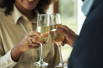 Young adult Black woman and young adult Black man clinking champagne glasses, smiling and celebrating together, close up on hands and faces, festive social gathering