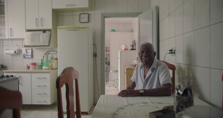 One Elderly Black man seated at a kitchen table, smiling warmly, exuding positivity and joy,...