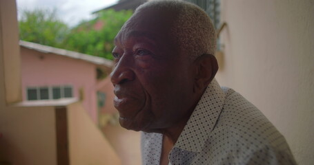 African American Elderly man sitting on porch smiling, showing wisdom and warmth, with a contemplative expression, surrounded by tropical residential background
