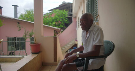 African American Elderly man sitting on porch smiling, showing wisdom and warmth, with a contemplative expression, surrounded by tropical residential background