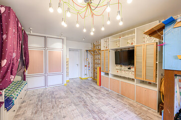 Bright, airy playroom features a large storage unit, playful lighting, and a child-friendly design. It has light wood flooring and colorful accents