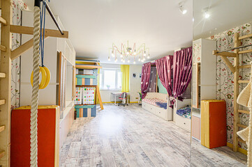 Bright, playful kids' room with gymnastic equipment, a bed with curtains, colorful storage, and a unique chandelier