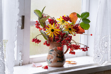 a bouquet of autumn flowers and leaves on window