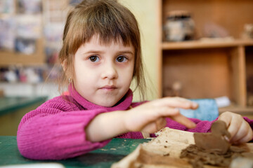 A preschool girl is engaged in clay modeling in a ceramics class. Every Saturday, the children are eager to go to their ceramics class and create pottery.