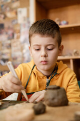 The boy is engaged in clay modeling in a ceramics class. Every Saturday, the children are eager to go to their ceramics class and create pottery.