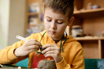 The boy is engaged in clay modeling in a ceramics class. Every Saturday, the children are eager to go to their ceramics class and create pottery.