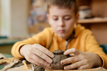 The boy is engaged in clay modeling in a ceramics class. Every Saturday, the children are eager to go to their ceramics class and create pottery.