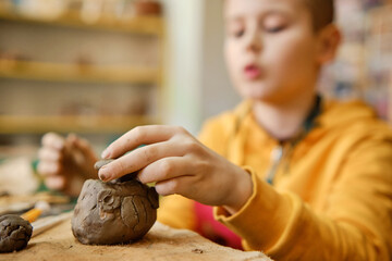 The boy is engaged in clay modeling in a ceramics class. Every Saturday, the children are eager to go to their ceramics class and create pottery.
