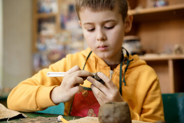 The boy is engaged in clay modeling in a ceramics class. Every Saturday, the children are eager to go to their ceramics class and create pottery.