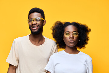 Obraz premium Happy African American couple wearing trendy glasses against vibrant yellow background, showcasing fashion and cheerful emotions, perfect for contemporary lifestyle themes