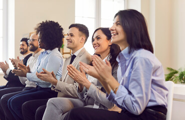 Group of happy joyful business people applauding to speaker sitting in a row in meeting room. Successful coworkers and company employees clapping a colleague on business training or conference.