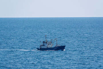 Fishing boat in blue sea and clear sky with birds flying overhead.