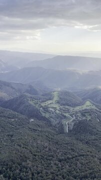 Panoramic view taken from Mirador del Far, near the medieval village of Rupit. A landscape of mountains, hills, and valleys covered in forests, with green areas illuminated by the sunset light. Spain
