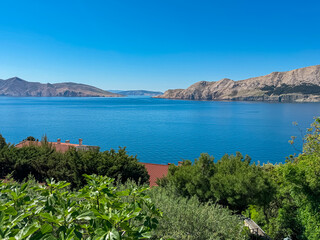 Stunning panoramic view of the deep blue Adriatic Sea and the rugged coastline of Ba&scaron;ka on Krk island, Croatia, seen from above with lush green trees and a clear sky on a perfect sunny summer day.