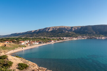Fototapeta premium A beautiful panoramic view of the entire Baška bay on Krk island, Croatia, featuring the long Vela Plaža beach and the charming coastal town set against a backdrop of rolling hills.