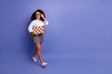 Smiling young woman with natural hair holding a chessboard on a purple background expressing optimism and enthusiasm
