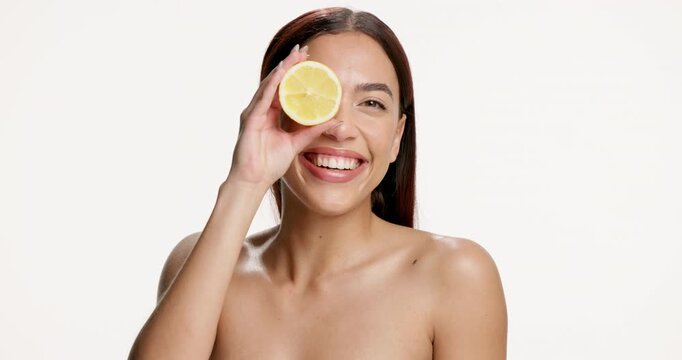 Face of woman, lemon and smile in studio for skincare, vitamin c and natural beauty for wellness. Portrait, happy person and dermatology with citrus fruit, skin glow and space on white background.