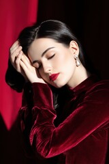 Fashion portrait of a model with elegant hairstyle, wearing cranberry velvet attire, showcasing beauty and sophistication against a rich, textured backdrop with soft lighting
