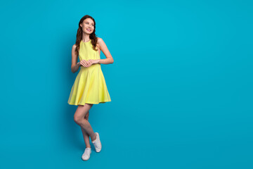 Stylish young woman in a bright yellow dress smiling confidently against a vibrant blue studio background