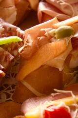 Canapé with prosciutto, melon, and olive, garnished with salami and vegetables, served on a festive table as a refined appetizer for a wedding banquet.