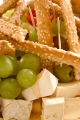  Assorted brie cheese with grapes and olives, decorated with sesame breadsticks, served as an appetizer on a festive table.