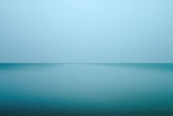 Calm waters meet a hazy sky, creating a minimal, serene landscape with a soft color palette