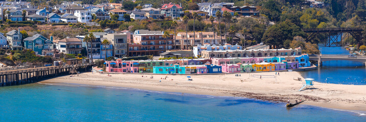 Aerial view of Capitola Beach in California, featuring pastel Venetian cottages, a wooden pier, a bridge over an inlet, and the Pacific Ocean.