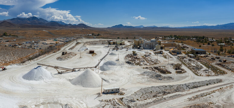 Aerial view of a salt mining site in Nevada featuring white salt mounds, industrial buildings, dirt roads, rail tracks, and a vast desert landscape.
