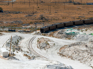 Aerial view of a salt mining site in Nevada featuring white salt mounds, a long freight train,...
