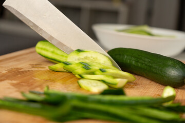 Slicing cucumbers with a large knife on wood cooking board close-up