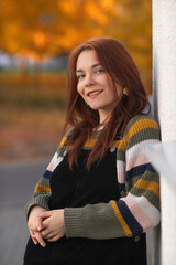 Young woman with glasses, holding vibrant autumn leaves, stands in a sunlit outdoor setting, surrounded by colorful foliage, capturing the essence of fall and nature's beauty