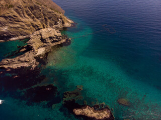 Aerial view of rugged coastal cliffs and crystal-clear turquoise waters with submerged rocks and coral formations