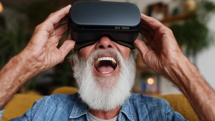 A man with a beard and gray hair is wearing a virtual reality headset and smiling. He is sitting on a couch and he is enjoying the experience - Powered by Adobe