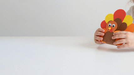 Child holding handmade paper turkey craft on white background (copy space)