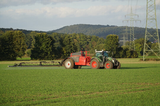 Agricultural landscape with a colourful tractor spraying a crop field. Evening sun near Goettingen, Lower Saxony, Germany.