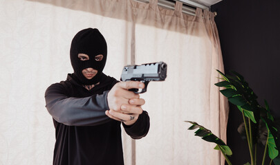 A hooded robber with a gun breaks into a house.