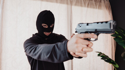 A hooded robber with a gun breaks into a house.