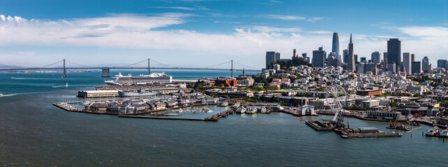 Aerial view of San Francisco featuring the downtown skyline, Salesforce Tower, Transamerica Pyramid, Bay Bridge, waterfront piers, and ferris wheel.