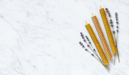 Three twisted beeswax candles with a honeycomb texture and lavender sprigs on a copy space marble surface. Spa and relaxation concept.