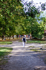 girl walks along the path, with a black backpack, autumn yard, rear view, trees, pigeons in the grass, playground, sun, autumn, outdoors, sunny, vertical photo