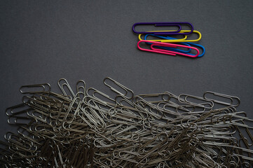 A vibrant contrast of colorful paper clips against a pile of metallic ones on a dark background. Highlights individuality, organization, and a pop of creativity in office supplies