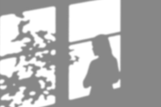 Mysterious shadow figure seen through a window frame casting intriguing light and dark patterns indoors