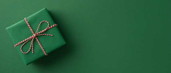 A neatly wrapped green gift with red and white twine sits on a solid green backdrop, conveying holiday gifting, festive charm, and seasonal greetings for Christmas and New Year campaigns