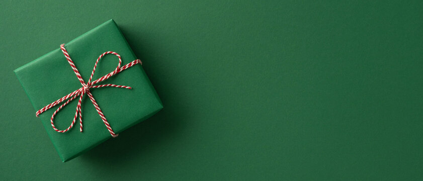 A neatly wrapped green gift with red and white twine sits on a solid green backdrop, conveying holiday gifting, festive charm, and seasonal greetings for Christmas and New Year campaigns