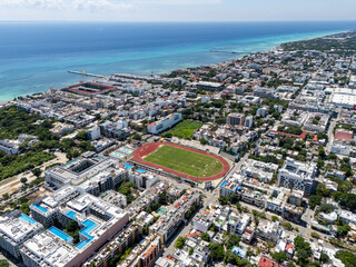 Fototapeta premium Aerial drone view of downtown area in Playa del Carmen with buildings and stadium and blue Caribbean Sea in the background on a summer day 