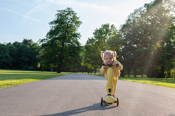 Scooter child. Girl riding scooter toddler. Yellow outdoor activity park road.